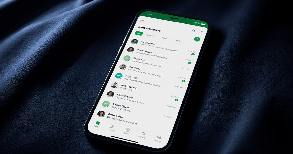 Smartphone on dark navy fabric showing a WhatsApp CRM conversations dashboard with multiple team chat threads